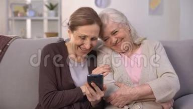 快乐的老女人看着智能手机上的照片，笑着，美好的回忆